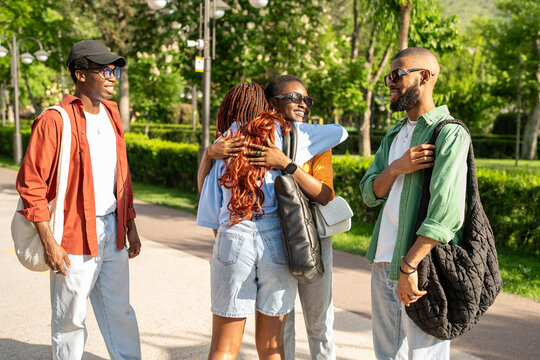 Excited happy group of African university students cheerfully greeting one another with hugs outside in park. Black friends congratulating of finals, laughter clapping, friendly meeting together 