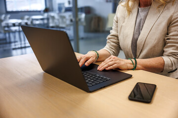 Woman entrepreneur typing on laptop while working at office desk, mobile phone within reach. 