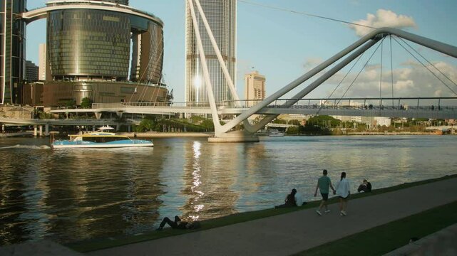 view of Neville Bonner Bridge stretching over the river, people wandering the vibrant waterfront