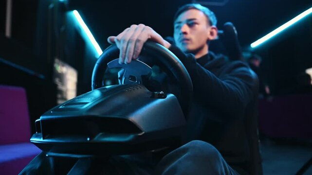 In the seat. Young guy is playing racing game by using driving simulator.