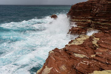 Red rock cliff in Cala Rossa, Terrasini, coastal landscape with waves crashing on red rock cliffs.