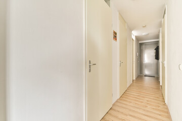 A sleek, modern corridor featuring minimalistic white walls and a wooden floor. The unobtrusive design emphasizes simplicity and spaciousness.