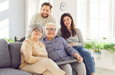 Happy family portrait with parents and adult children embracing together on the sofa at home. They...
