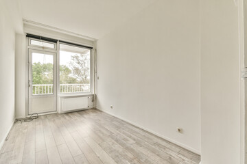 An empty room featuring large windows allowing ample natural light. The light wooden flooring complements the clean, white walls, creating a serene atmosphere.
