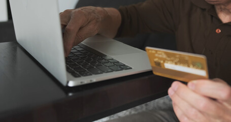 Hand of senior male buying online with credit card. Man using laptop and doing online transactions at home. Concept online shopping, technology and lifestyle, buying cryptocurrency