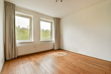 An empty room featuring large windows that allow natural light to illuminate the wooden floor,...