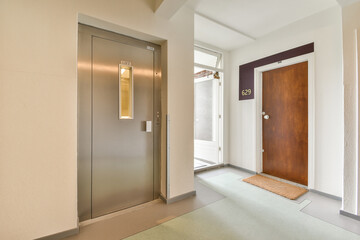 A sleek entrance hallway featuring an elevator and a wooden door, modern design elements, and smooth flooring create a welcoming atmosphere.