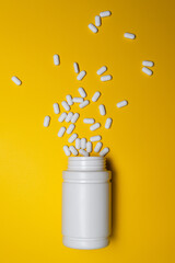 White Pills Spilling from Bottle on Bright Yellow Background