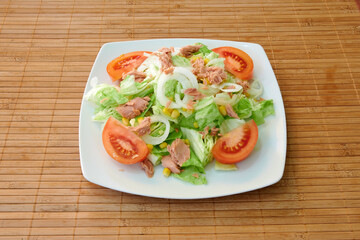 A plate of salad with tomatoes, lettuce, and onions. The salad is served on a wooden table