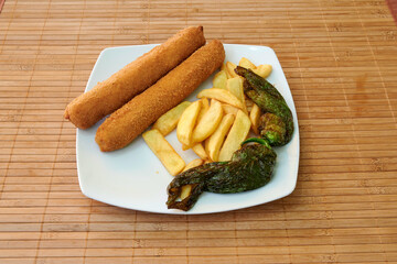 A plate of fried chicken and french fries with a green pepper on top. The plate is on a wooden table
