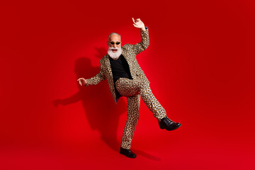 Energetic elderly man in leopard print suit dancing joyfully on a vibrant red background showcasing style and happiness