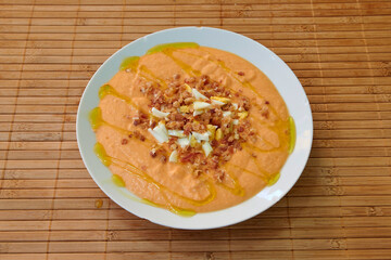 A white plate with a delicious red soup topped with bacon bits. The bacon is spread out across the surface of the soup, creating a visually appealing presentation