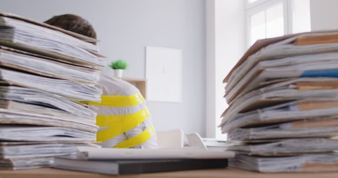 Bookkeeper escaping from workplace. Funny man who has become office slave, fastened to chair with scotch tape, sitting by desk with paperwork, cautiously looks around and starts stealthy movement out