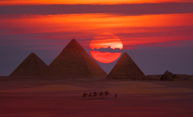 Camel caravan in front of the Great pyramid of Giza complex at red sunset - Cairo, Egypt