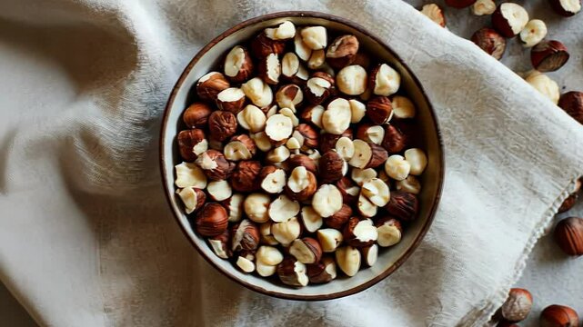 A bowl of shelled hazelnuts and scattered whole nuts on a linen cloth.