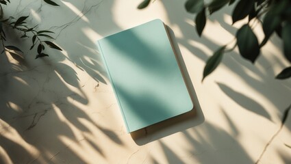 Aesthetic minimalist company branding mockup featuring a closed notebook with a blank cover on a table, enhanced by natural floral sunlight shadows.