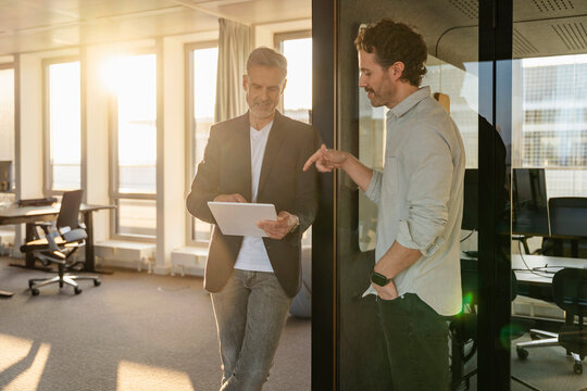 Two men having a business meeting in an office at sunset with a tablet