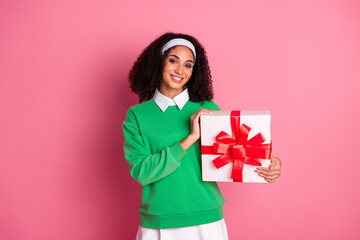 Smiling woman in green jumper with gift box posing against bright pink background
