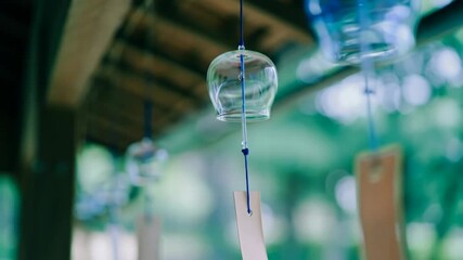 Japanese glass wind chime (Furin) hanging under eaves footage, blurred green background. Symbolizing summer traditions, tranquility and gentle sounds in Japan. Scene of peaceful garden atmosphere.