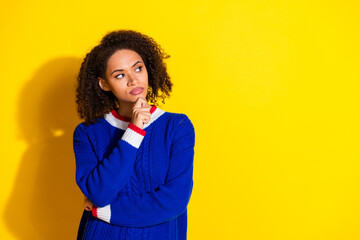 Young woman in vibrant blue sweater contemplating an idea against a bright yellow background