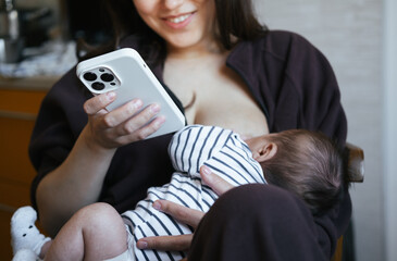 Beautiful young woman is breastfeeding her baby boy at home, close-up view. She is working online at the same time, remote work from home. Chatting with friend, having online shopping. 