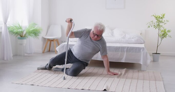 Unhealthy senior man stands up from the floor after a fall caused by an accident or health problem at home. Man struggles with injury or disease, highlighting the dangers of trauma for elderly people.