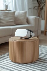 A white VR headset sits on a stump coffee table in an open-plan living room that features a gray sofa