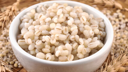 Cooked peeled barley grains in white bowl on wooden table