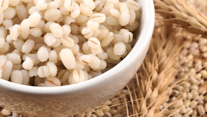 Cooked peeled barley grains in white bowl on wooden table