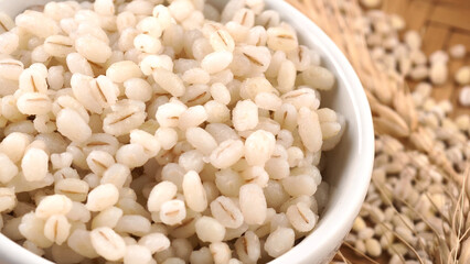 Cooked peeled barley grains in white bowl on wooden table