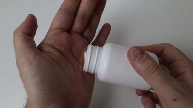 Hands on white background pour 2 pills back into the white jar and screw the lid on