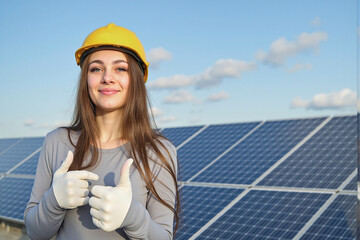 Happy Female Engineer in Yellow Hard Hat and Gloves Showing Double Thumbs Up at Solar Power Plant.