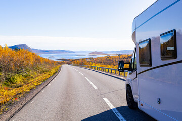 Motorhome driving on a scenic road in Kiruna, Sweden, with autumn foliage and beautiful lake views.