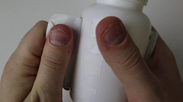 Fingers tear the label off a white jar on a white background