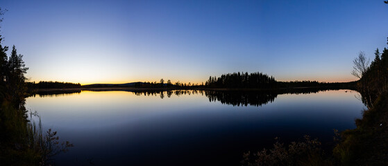 A peaceful sunset over a lake in Lapland, Sweden, with the reflection of trees in the still water.