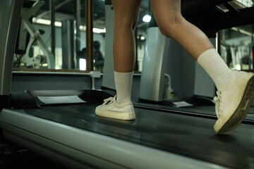 Fototapeta premium Close-up of a woman’s legs walking on a treadmill at the gym. Focus on fitness, routine, and cardio training
