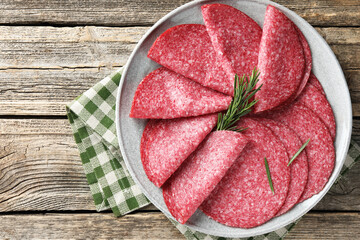 Slices of delicious sausage with rosemary served on wooden table, top view