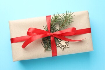 Gift wrapped in kraft paper with bow, ornament and fir tree branch on light blue background, top...