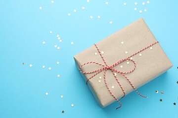 Gift wrapped in kraft paper and confetti on light blue background, top view
