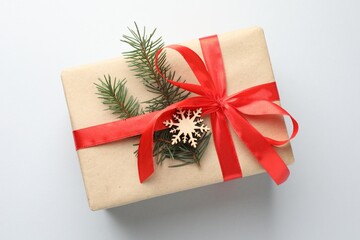 Gift wrapped in kraft paper with bow, ornament and fir tree branch on light background, top view