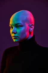 Close up portrait of young pretty woman with bald head posing looking forward in bright neon light against gradient background, showing confidence. Concept of beauty, fashion, style, equality.