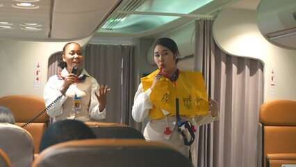 Asian stewardess safety explaining passengers prior to flight take off in airplane, air hostess uniform safety demonstration presenting pre-flight safety instructions life vest in emergency situation