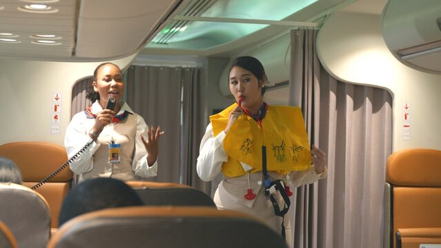Asian stewardess safety explaining passengers prior to flight take off in airplane, air hostess uniform safety demonstration presenting pre-flight safety instructions life vest in emergency situation