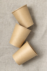 Disposable beige paper cups on a beige linen cloth top view, mockup. No plastic lifestyle