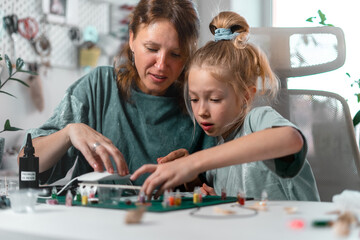 Little girl and her mother happily crafting colorful resin figures together at home. Family sharing...