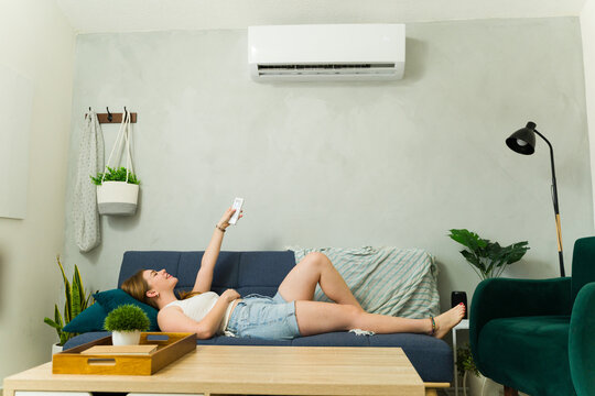 Woman relaxing on sofa using remote control for air conditioner