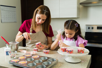 Little girl and her mom baking and decorating cupcakes together in kitchen