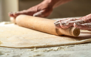 Person preparing a dough with a rolling pin. Female hands roll out a dough with a rolling pin. Closeup of man rolling dough with rolling pin for homemade bakery at table