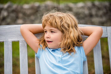 Child relaxing on the bench after long school day. Young boy sitting on the bench, pleasure. Children outdoor. Kids, idea and smile with a happy boy outside. Kid resting in summer park