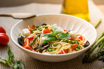 Pasta primavera spaghetti close up with cherry tomatoes, black olives, feta cheese and basil, served on wooden table, with natutal light, italian dish and cuisine homemade